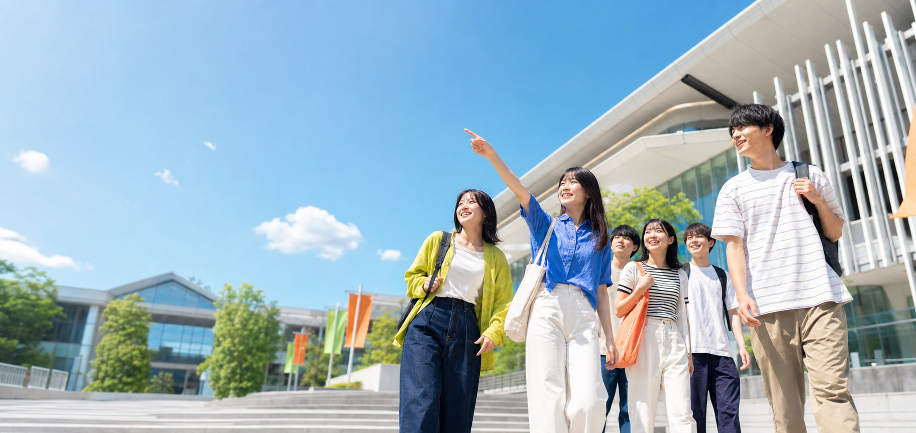 青空の大学キャンパスを見学する高校生たち
